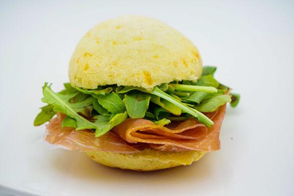 Pao de Queijo Slider. Hot honey, Prosciutto, Dressed greens with balsamic glaze served on a warm Brazilian cheese bread slider.