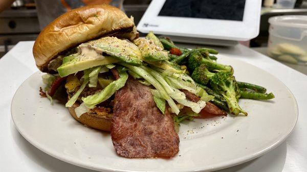 Turkey burger with turkey bacon, avocado and jalapeños alongside grilled vegetables.