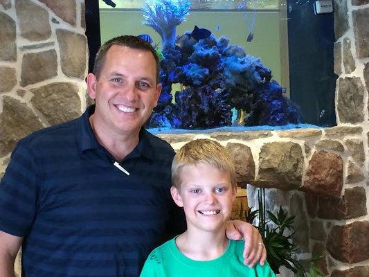 Dr. Packard with patient who just got his braces off - standing in front of the big fish tank located in the PFO waiting room in McKinney.