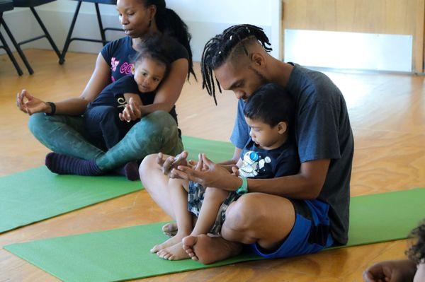 Parents sharing the SA-TA-NA-MA meditation with their children during kids jamm family yoga at Arts + Public Life.