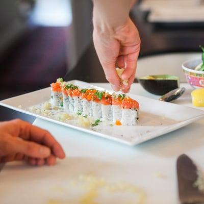 Putting crunchies on top of a spicy Dragon roll - red crab meat, cucumber and avocado topped with spicy tuna, tobiko and green onions.