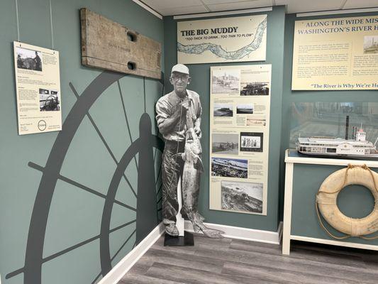 River exhibit featuring a graphic of a steamboat wheel, an image of a man with a sturgeon, life preservers, and a model of a snag boat