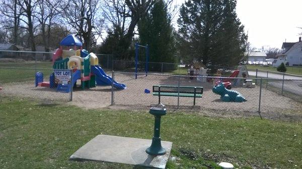 a fenced playground for tots with a water fountain right outside