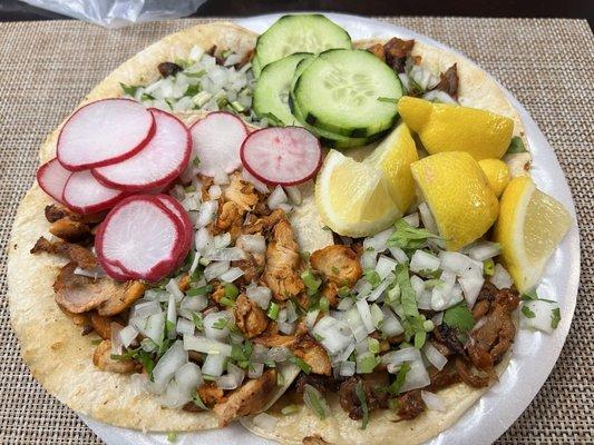 Al pastor and chicken tacos with sides of cucumber, radish, and lemons.