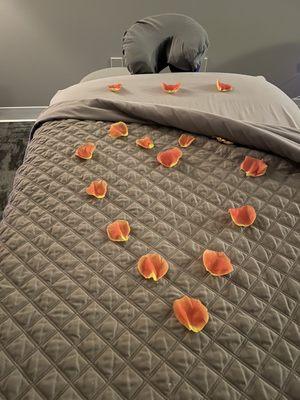 Heated, cozy massage table with rose petals shaped in a heart.