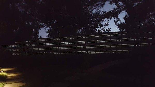 Stained cedar wood fence with rope lighting behind the planks. Custom design