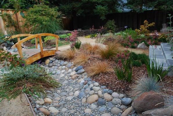 Japanese themed garden in Palo Alto featuring a wooden bridge over a dry creek, "deer chaser" fountain, and low-water plants.