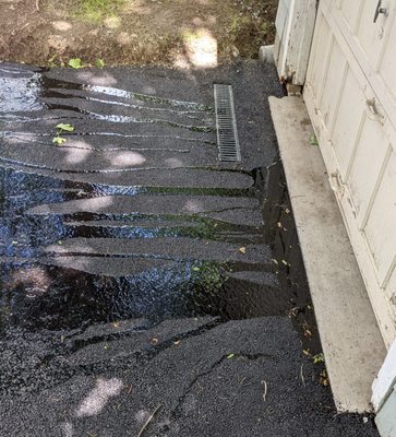 Water pooling in front of garage door due to improper placement of drain segment and poor grading of new driveway.