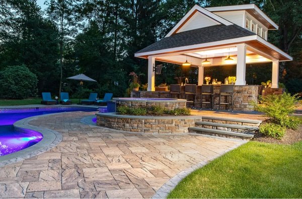 luxurious outdoor oasis featuring a custom pool, patio, hot tub, outdoor kitchen, and bluestone designed steps surrounded by plantings.