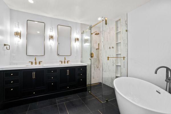 Modern bathroom remodel with a freestanding tub, glass shower enclosure, black vanity, gold fixtures, and elegant lighting accents.