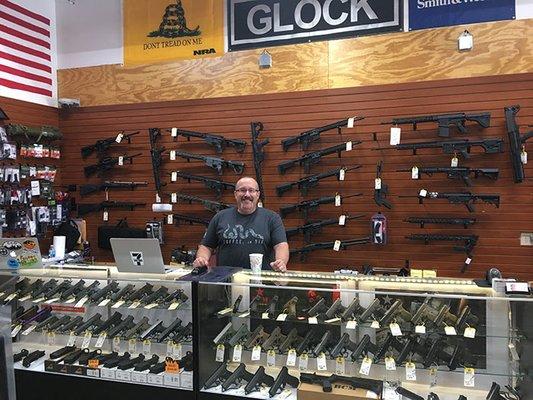 Chris at the Wall of Freedom with our selection of AR-15s and pistols suitable for concealed carry.