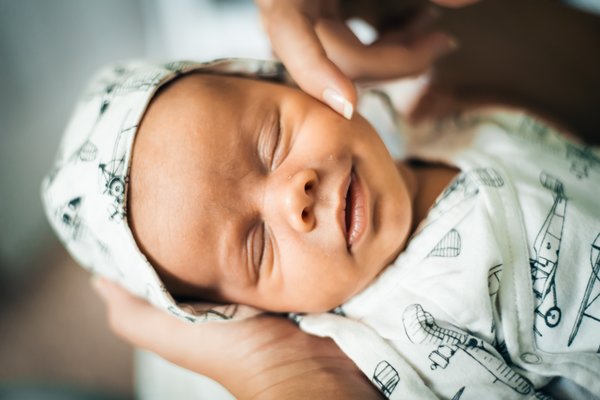 Newborn boy smiles in his sleep as his mother gently runs her finger over his cheek.