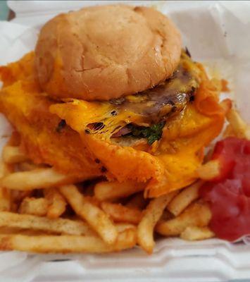 Huge cheeseburger with a skirt of cheddar cheese and crispy fries.