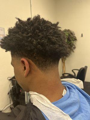 Low skin taper fade with disconnected curly scissor cut on top.