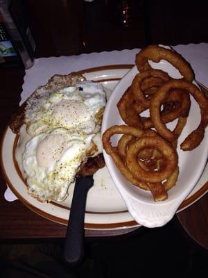 Chicken fried steak and two eggs with onion rings.