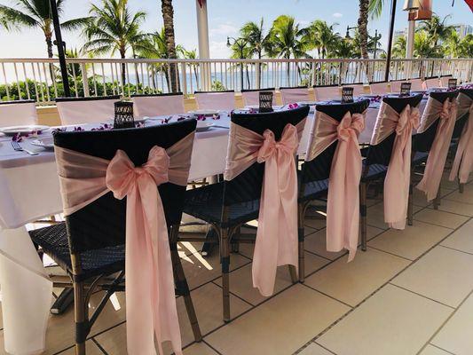 Simple pretty pink sashes adds a sweet touch to these wicker chairs attire Tiki's Grill and Bar!