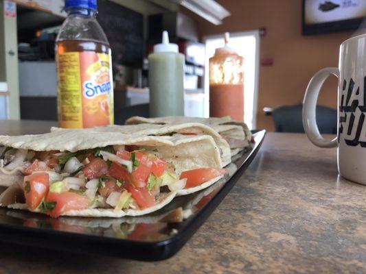 Delicious Pork tacos made with handmade tortillas with some spicy sauce on the side