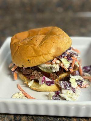 The PDG Sandwich! Grilled bun with your choice of meat, sauce, pickles, and then topped with our Housemade Coleslaw!