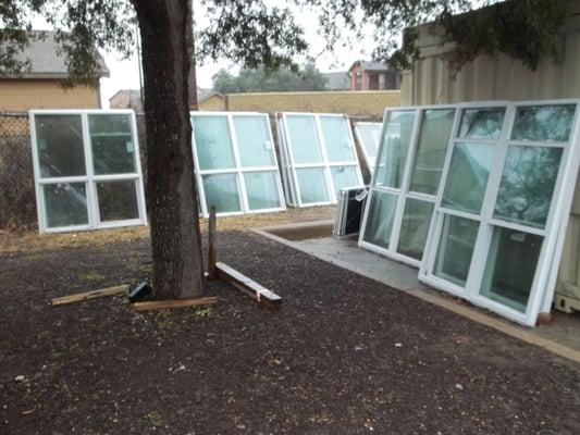 New" windows stacked outside in the rain next to dumpsters.