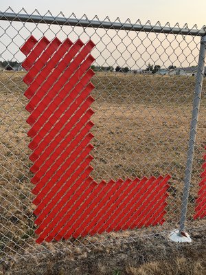 Fence art of the snap-in-place ribbon type spelled out "Learn Today Lead Tomorrow".