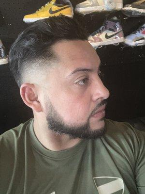 Low skin fade with comb back hair cut and beard.