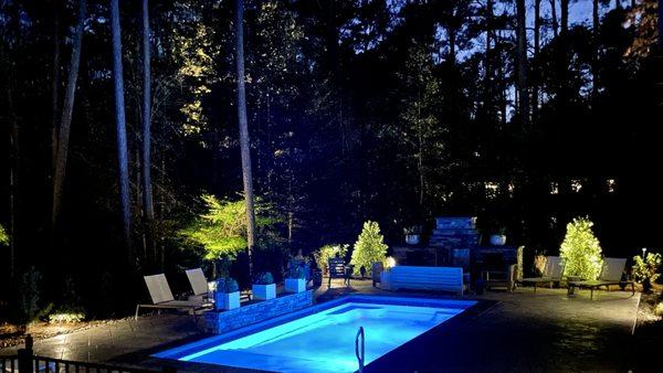 A pool, patio, and outdoor kitchen lit up at night.