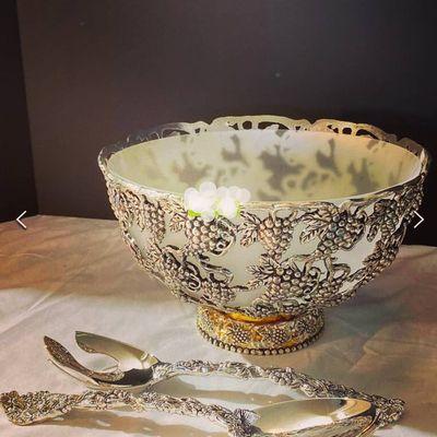 Silver serving bowl and serving utensils decorated with grapes and wine.