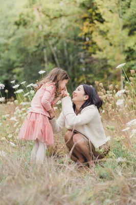 a mother sweetly touches her daughters nose in a field of wild flowers of queen Ann's lace