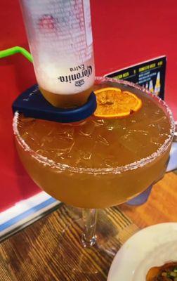 A bowl of margarita mix with corona and a dried orange.