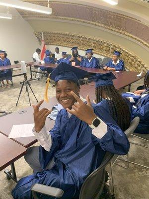 One of our founding 8th grade students smiles for a picture at our 2022-2023 Promotion Ceremony wearing a cap and gown!