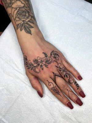 Delicate fine line floral hand tattoo with some sacred symbols