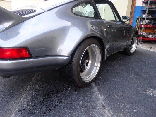 Porsche 911---with added flares, new wheels, and ducktail---sitting outside shop entrance.