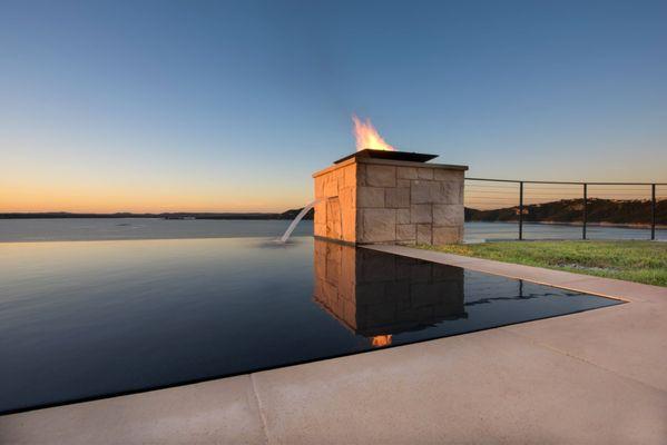 Stainless steel infinity edge pool with water feature overlooking natural water