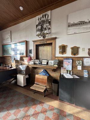 Old train ticket counter with a child's classroom desk in front.