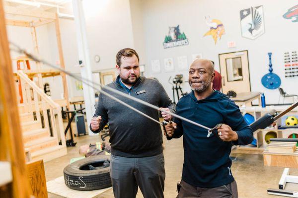 Occupational therapist instructing shoulder and upper back stabilization exercises in St. Paul clinic industrial rehab gym.