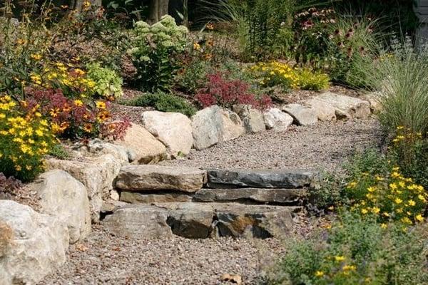 The natural boulder retaining wall and steps along with the gravel make this a casual garden that flows up the slope.