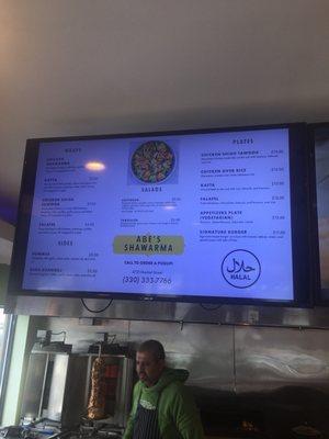 Menu board with Abraham the proprietor in the foreground and the chicken shawarma in the background.