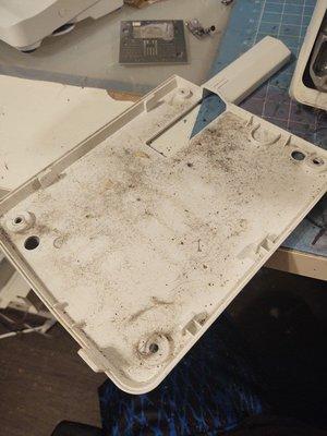 The bottom cover of the machine, covered in dust and lint after his "servicing"