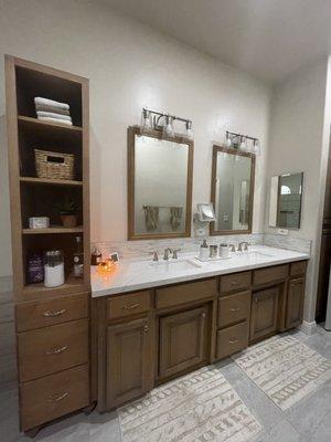 A remodeled master bath with a double sink and shelving.