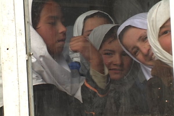 Afghan girls watch through the window as their school gets their first library.