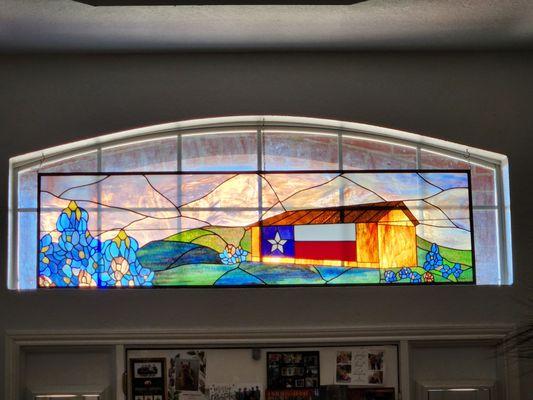 Stained glass transom panel Texas field of bluebonnets with a barn impressively displaying the Texas flag.