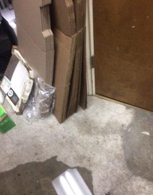 Water coming out of the restroom with pizza boxes on the ground