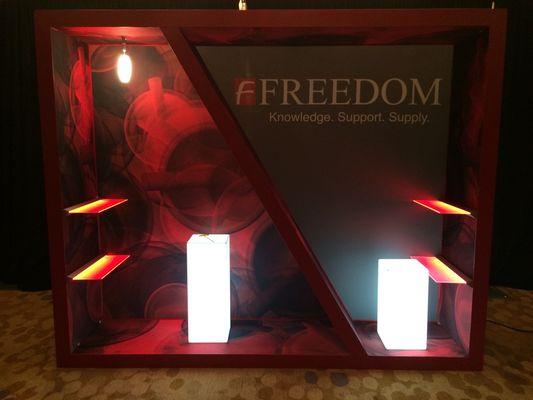 10x10 Custom envoy booth with powder coated extrusions, LED lit shelves, fabric graphics, and lit podiums.