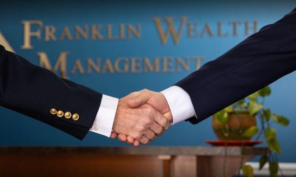 Two financial advisors shaking hands at Franklin Wealth Management office.