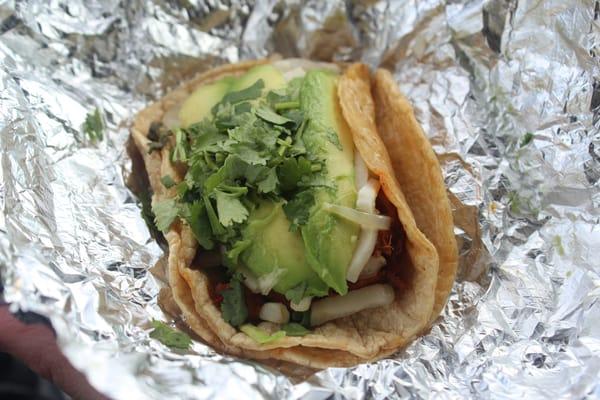 Corn taco with carnitas, cheese, avocado, cilantro and onions