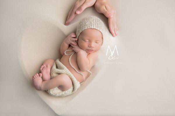 Newborn in heart with parent's hands wrapped around