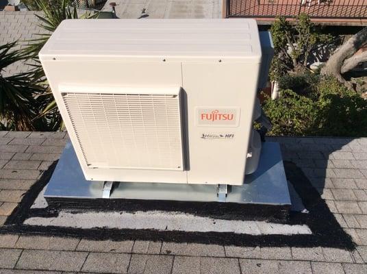 Ductless Fujitsu AC unit installed on a residential roof with sheet metal cover platform