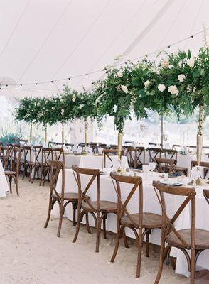 wedding tent with cross-back chairs and greenery center pieces